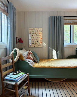 Cozy bedroom with green bed, wooden chair, alphabet poster, and two windows with blue curtains