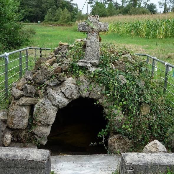 Old stone arch tunnel with ivy and a stone cross in a grassy rural area