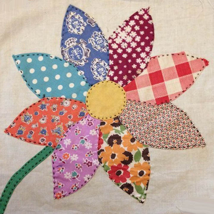 Quilted flower with eight patterned fabric petals in various colors around a yellow center button