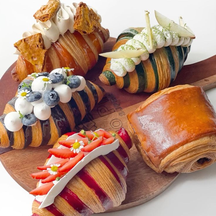 Five decorated croissants with cream, berries, and colorful stripes on wooden board