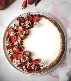 Round cream tart topped with strawberries and small white flowers, viewed from above