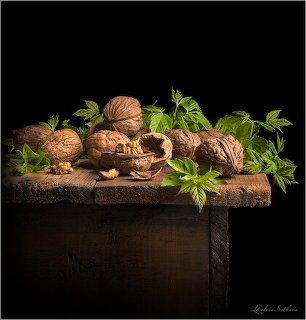 Whole and cracked walnuts with green leaves on a rustic wooden table against a black background