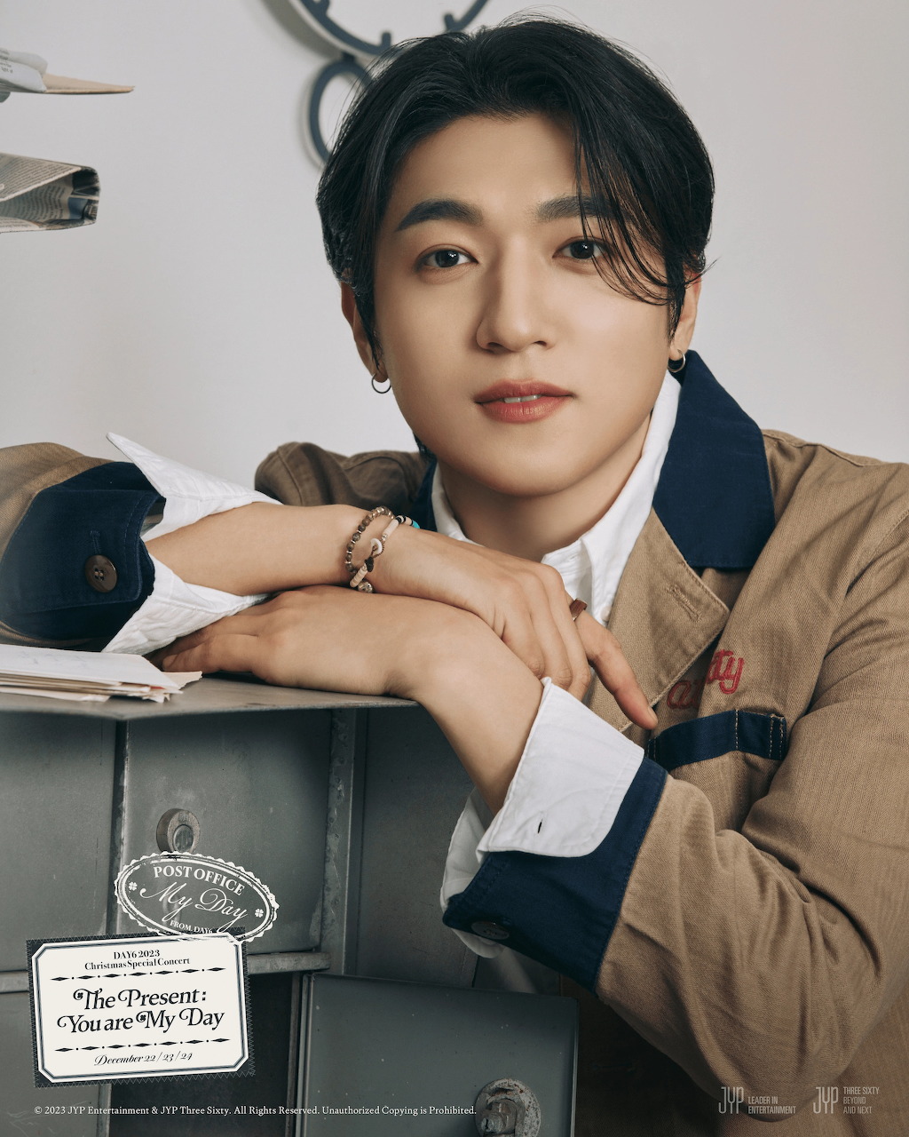 Young Korean man in tan blazer and white shirt leaning on a vintage prop surface, studio portrait