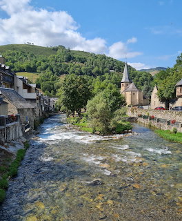 River flowing through Arreau village with stone buildings, church spire, and green hills in France