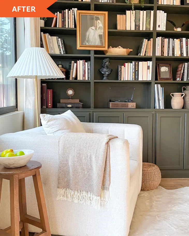 Large white armchair with cream throw in front of dark green built-in bookshelves filled with books