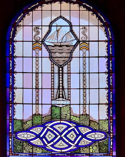 Arched stained glass window with blue knotwork and a central hanging basket motif
