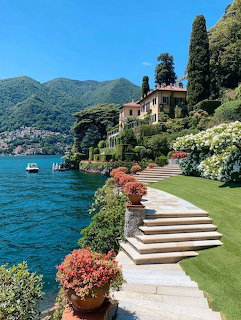 Lakeside villa with terraced garden, stone steps, flowers, and cypress trees by blue water