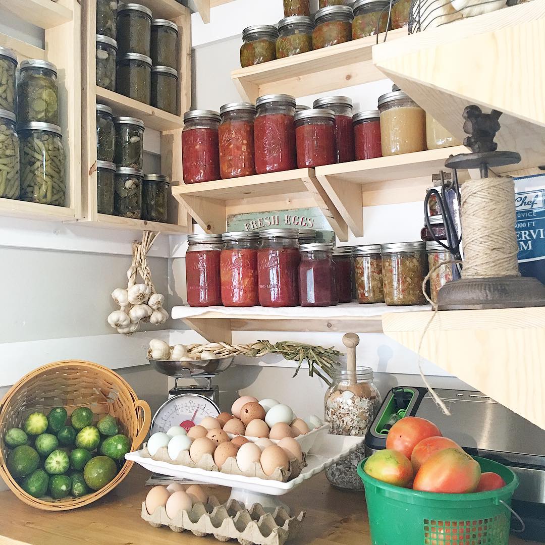 Organized white corner pantry shelves with glass jars and produce baskets