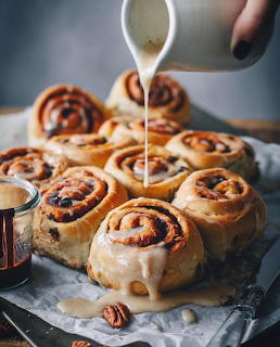 Pecan cinnamon rolls being drizzled with white glaze on parchment paper