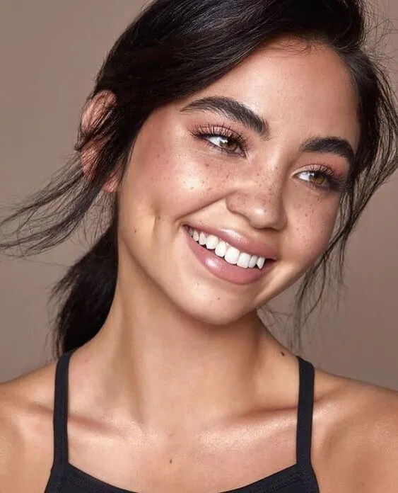 Young woman with freckles and natural makeup smiling at the camera