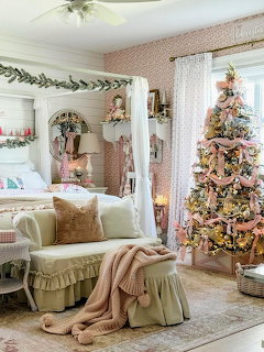 Cozy bedroom with pink decorated Christmas tree, white loveseat with knit throw, and garland over bed