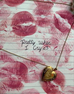Pink lipstick kiss stains on white wood background with gold heart locket necklace and handwritten note