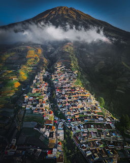 Aerial view of village below misty volcanic mountain with colorful houses and green slopes
