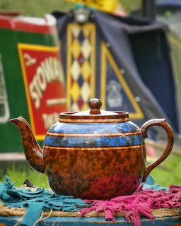 Vintage brown glazed teapot with blue decorative band on colorful fabric with canal boat behind
