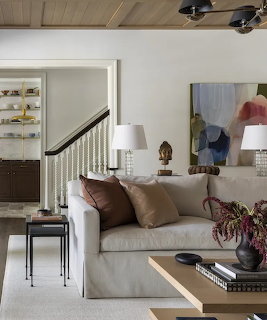 Elegant living room with white sofa, brown pillows, table lamps, abstract painting, and staircase