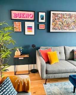 Modern living room with teal wall, gray sofa, colorful pillows, framed art, and houseplants