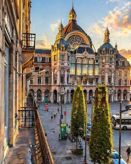 Ornate Antwerp Central Station facade with dome and towers at sunset, trees lining the plaza