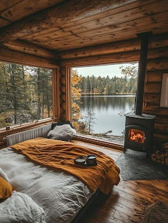 Rustic log cabin bedroom with lake view through large window, bed with striped blanket, and wood-burning stove