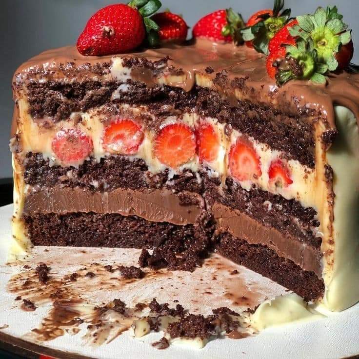 Slice of layered chocolate cake with strawberries and chocolate frosting on a white plate
