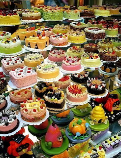 Colorful assortment of decorated cakes and pastries displayed in rows at a cake shop