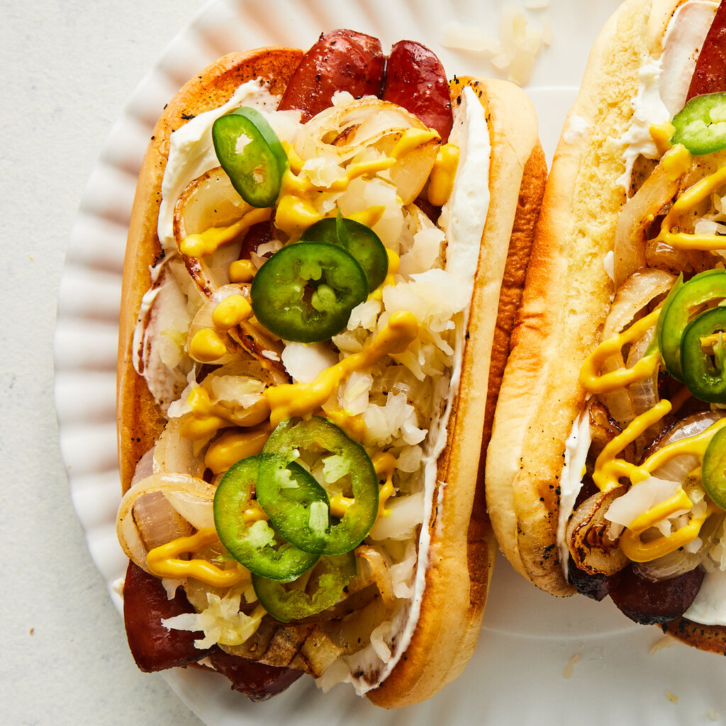 Two hot dogs loaded with cheese, onions, jalapeños and sauce on a plate