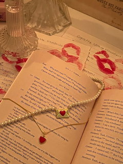 Open book with pearl necklace, red heart charms, kiss marks, and vintage perfume bottle on aged pages