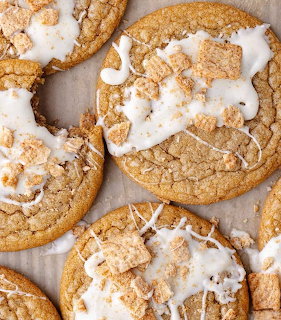 Golden brown cookies with white icing drizzle and cinnamon cereal toppings on parchment paper