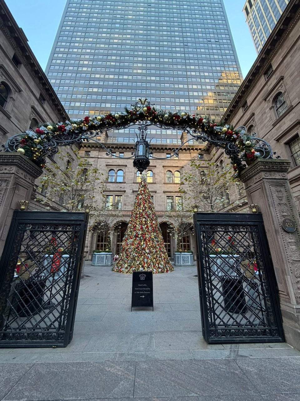 Christmas decorations with lit tree and garland arch in city plaza with tall buildings
