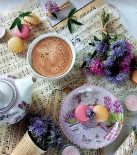 Flat-lay of hot cocoa, colorful macarons, purple flowers, and a teapot on sheet music