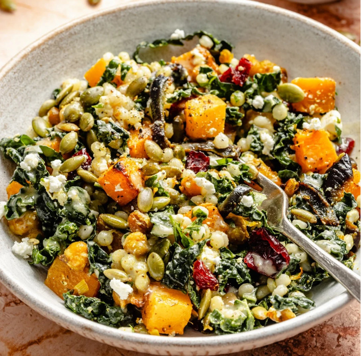 Bowl of couscous salad with butternut squash, kale, cranberries, pumpkin seeds, and feta cheese