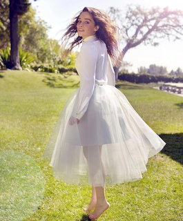 Woman in white dress twirling on green lawn under sunny sky