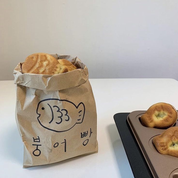 Fish-shaped taiyaki pastries in paper bag with fish logo and two on dark tray