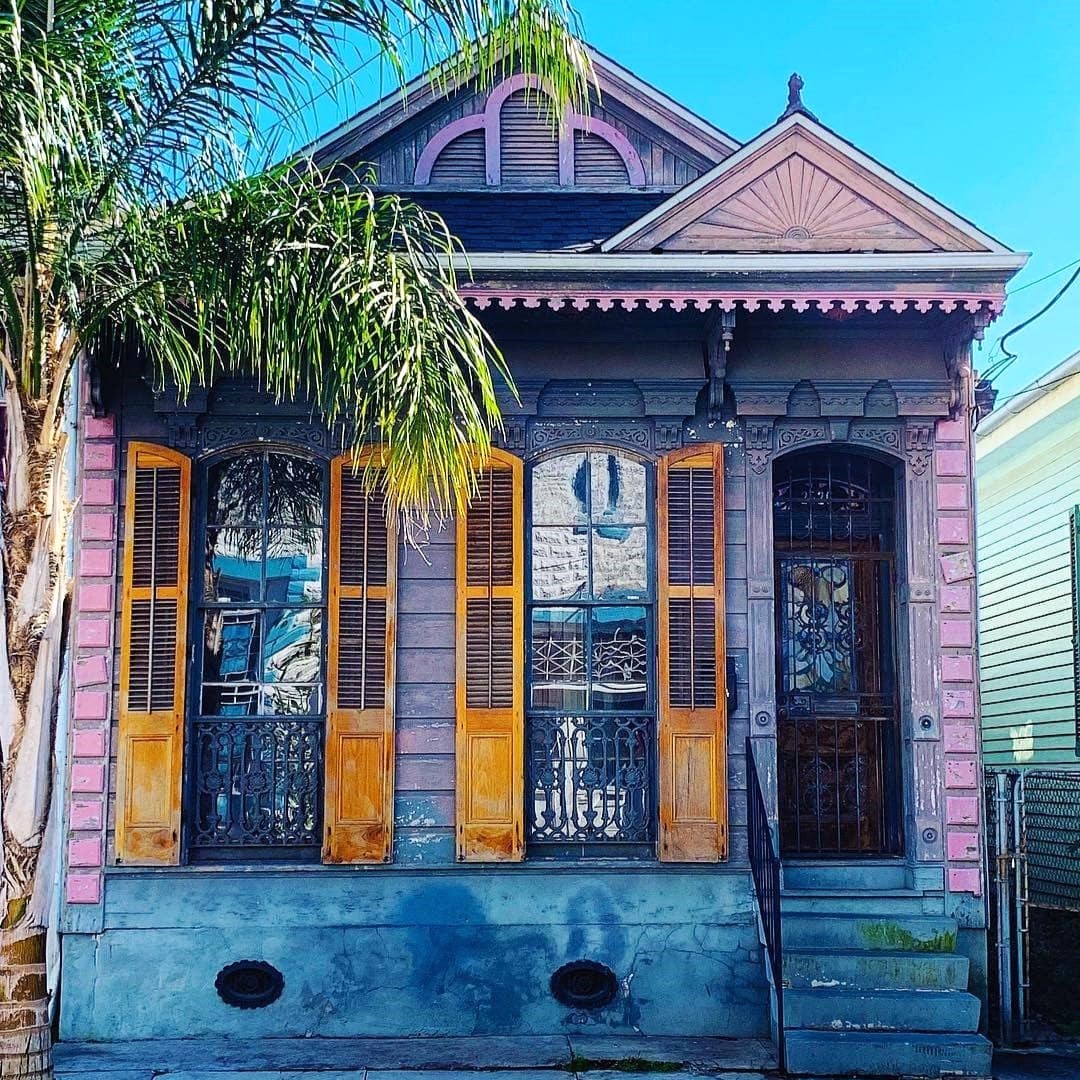 Colorful Victorian shotgun house with purple trim, yellow shutters, and ornate ironwork