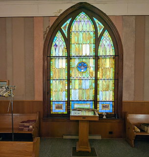 Stained glass church window above a lectern inside a chapel with wooden pews