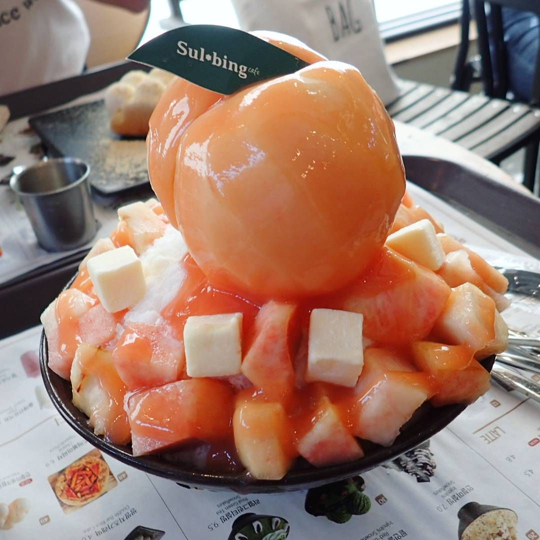 Peach shaved ice dessert topped with a whole peach and diced fruit cubes