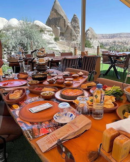 Breakfast table with tea, bread, and dishes on a terrace overlooking rocky hills