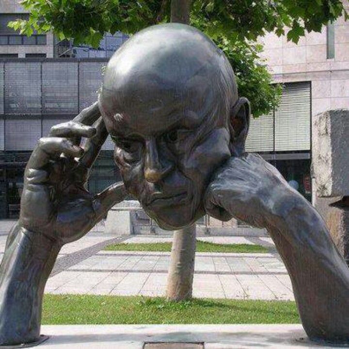 Bronze sculpture of crouched figure with hands on head in outdoor plaza