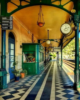 Colorful vintage train station platform with green pillars, checkered floor, yellow canopy, and station clock