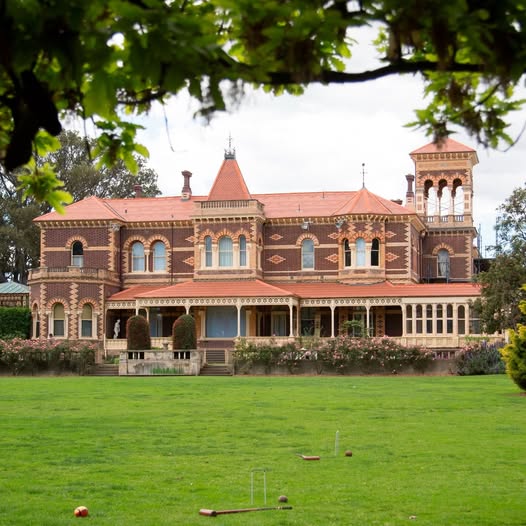 Large red brick Victorian mansion with corner tower and veranda on green lawn