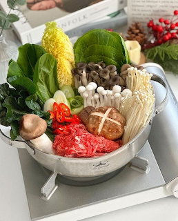 Metal pot with Korean hot pot ingredients such as mushrooms, greens, cabbage, beef, and red chili slices.