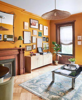 Living room with orange walls, wooden fireplace, gallery wall, white credenza, and blue area rug on hardwood floor