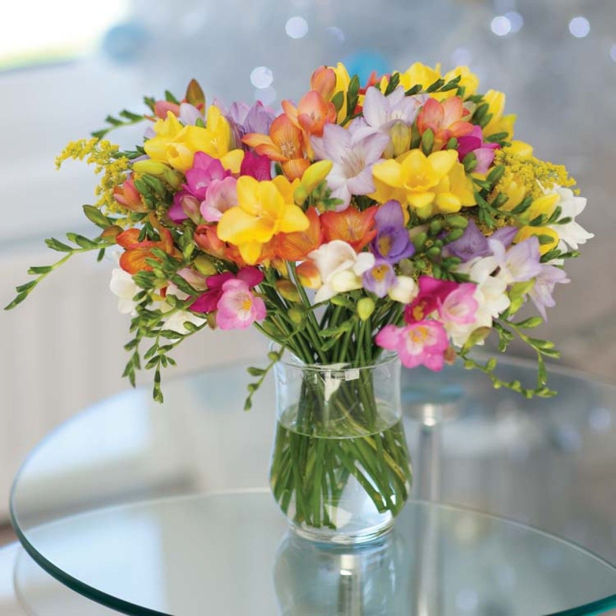 Colorful freesia bouquet in a clear glass vase on a round glass table
