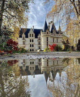 White French castle with spires reflected in a pond surrounded by autumn trees