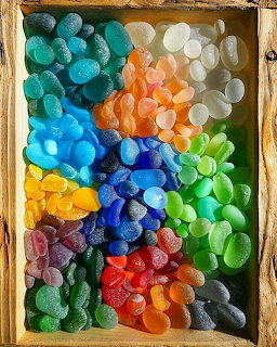 Rainbow-sorted sea glass pieces in wooden tray showing various colors from turquoise to purple