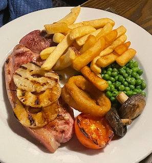Gammon steak dinner with chips, pineapple, onion rings, peas, and vegetables on white plate