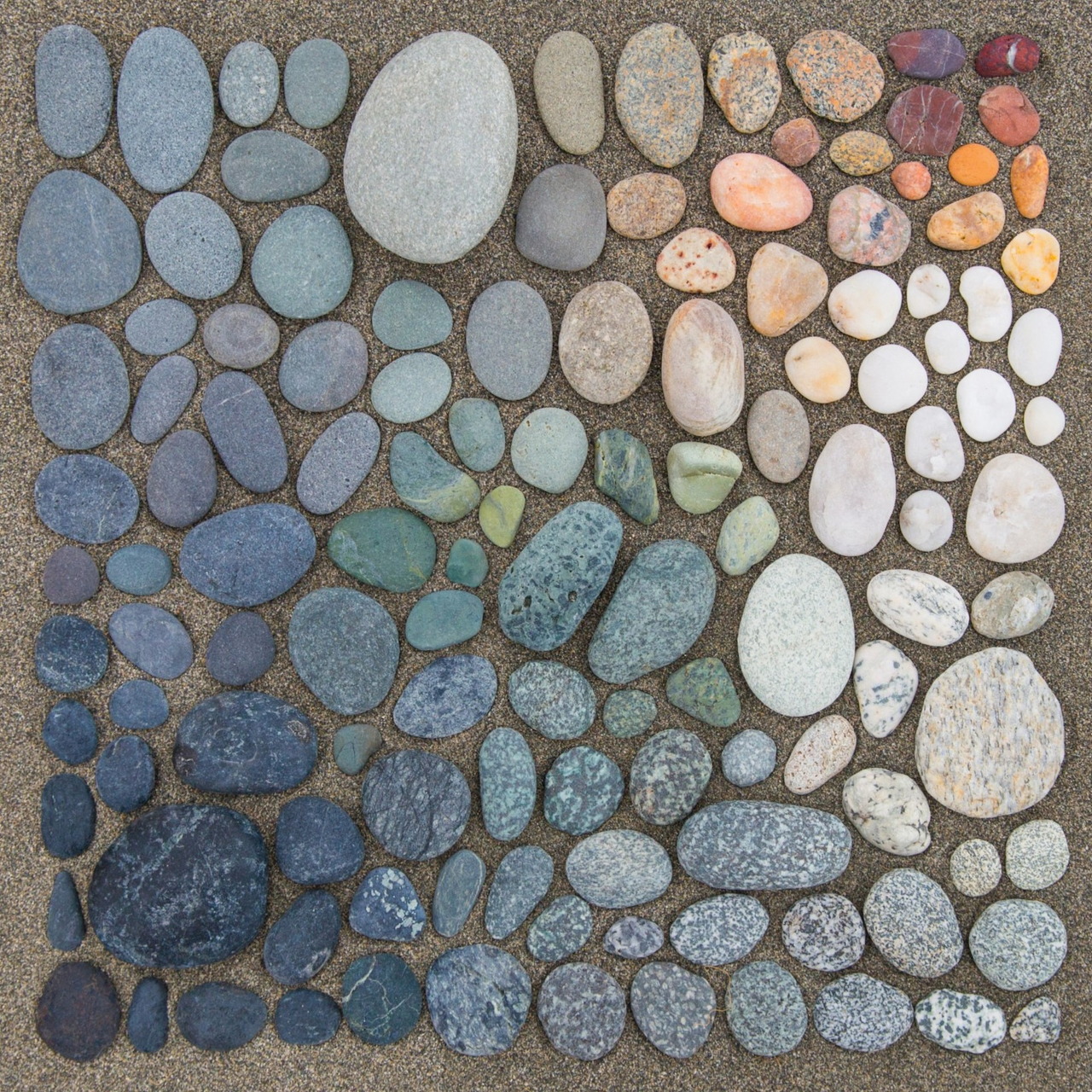 Oval stones arranged in a gradient mosaic from dark blue and gray to white and orange