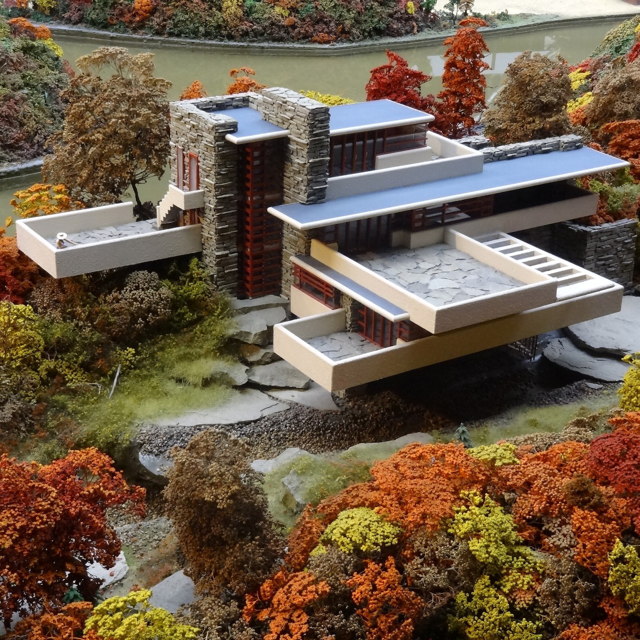 Model of a modern cantilevered house surrounded by autumn trees and a small stream