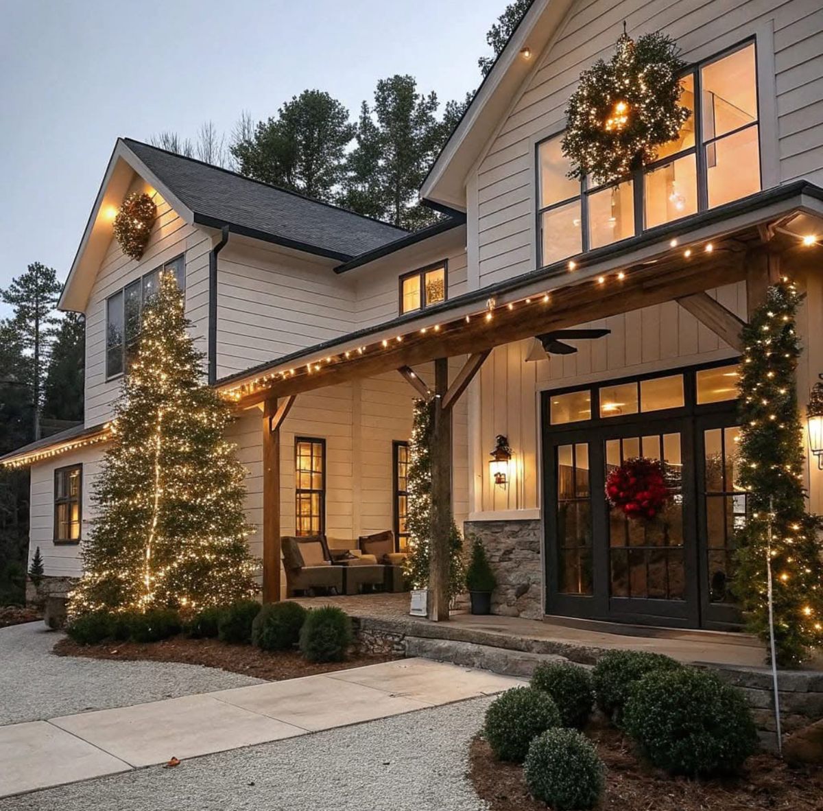 Two-story farmhouse with Christmas lights, wreaths, and decorated trees glowing at twilight