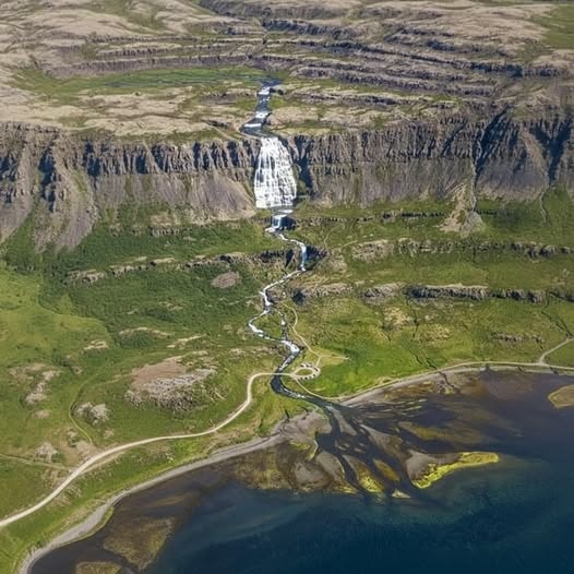 Aerial view of Dynjandi waterfall on steep cliffs above a coastal plain in Iceland