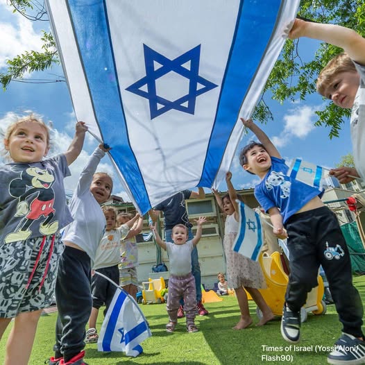 Group of children holding large Israeli flag with Star of David outdoors on sunny day